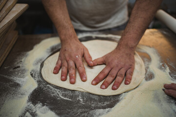 Baker man kneading pizza dough with his hands at the bakery kitchen