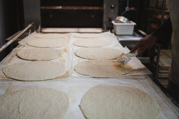Fototapeta na wymiar Baker man using perforation pizza dough base with roller in bakery