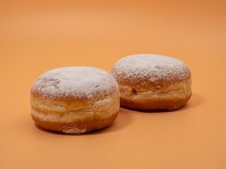 Freshly baked and dusted with powdered sugar German donuts. Donut berliner or krapfen on orange background.