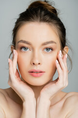 Young fair haired model with naked shoulders touching cheecks isolated on grey.