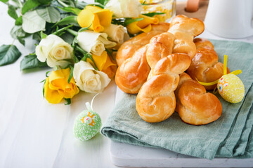 Easter breakfast Holliday concept. Easter bunny buns rolls with cinnamon made from yeast dough with orange glaze, easter decorations, colored eggs on white spring background. Easter Holliday card.