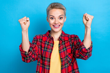 Photo of young overjoyed surprised student girl attractive woman wear checkered shirt fists up triumph victory isolated on blue color background