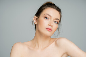 charming woman with natural makeup and naked shoulders looking at camera isolated on grey.