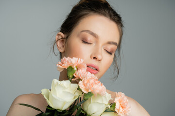 Young woman with natural makeup holding flowers isolated on grey.
