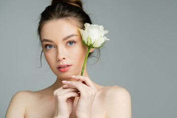 young woman with naked shoulders holding white rose and looking at camera isolated on grey.
