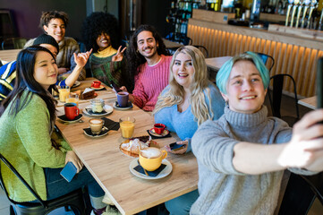 Young friends toasting coffee and doing breakfast in bar bakery shop, happy hipster people drinking cappuccino and eating cakes, friendship concept, focus on the blonde woman