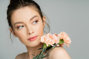 Pretty fair haired woman looking away near carnations isolated on grey.