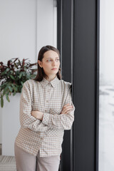 confident business woman stands at window in office looking into distance. thoughtful female lead project manager is thinking over work strategy. successful financial case marketer and CEO. work in