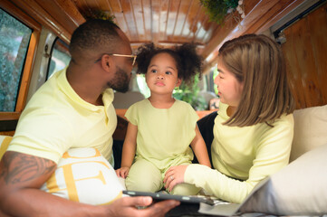The back of a white classic van, little kids play and learn about the world on their tablet with parents taking care of helping.