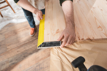 Cropped view of carpenter using square tool on wooden board.