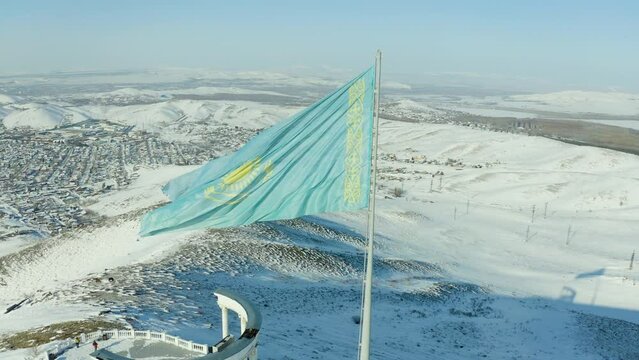 large flag of Kazakhstan fluttering in wind against the background of mountains and snow of the country's nature, a symbol of the republic
