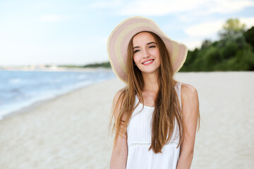 Portrait of a happy smiling woman in free happiness bliss on ocean beach standing with a hat. A female model in a white summer dress enjoying nature during travel holidays vacation outdoors