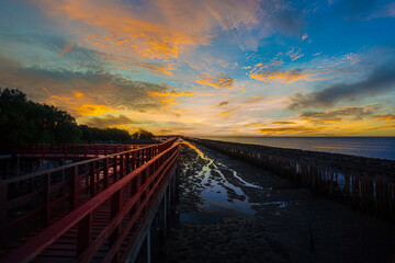 Fototapeta premium Scenery of the wooden bridge at sunrise,red wooden bridge and sea in the morning,In the morning the red bridge and the sun rise on the horizon. Bridge over the sea in Thailand Thai landscape.