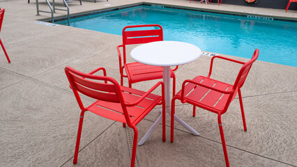 Empty patio table and chairs on the cement pool deck in red, white and blue colors