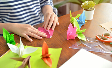 Female hands folding paper birds colorful as a hobby on a wooden table at home