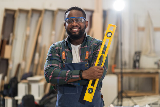 Portrait of African American male carpenter holding precision level making new furniture at wood workshop. Portrait of joiner male working with precision level in wood factory