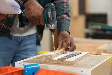 Hands of male carpenter using cordless drill making new furniture at wood factory