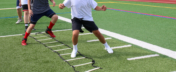 Young football players running in the ladder drill on a turf field