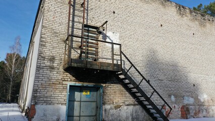 Old fireproof metal staircase in the backyard of an industrial brick building in black. Sign 