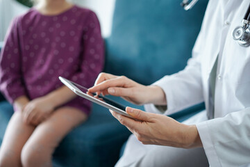 Doctor woman and kid patient at home. The pediatrician uses a tablet computer, close up. Medicine, healthcare concepts