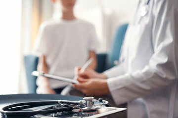Stethoscope lying on the tablet computer in front of doctor and kid boy patient at the background . Medicine, healthcare concept