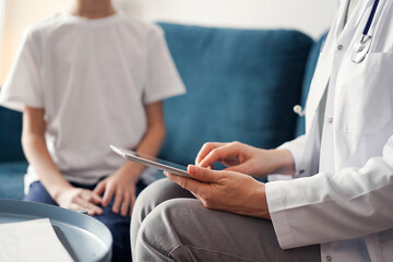 Doctor woman and kid boy patient at home. The pediatrician using tablet computer while filling up medical records, close up. Medicine, healthcare concepts