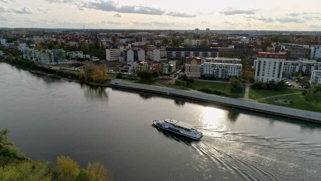 flight parallel to the river elbe in magdeburg, sunset with excursion boat on the elbe, sun reflection on the water, new buildings on the opposite bank