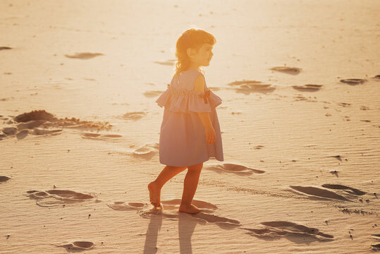 Back view of Child girl walk on the sand on the sandy beach. Little girl toddler playing and walking in the sand. The concept of family summer vacation with children outdoors.