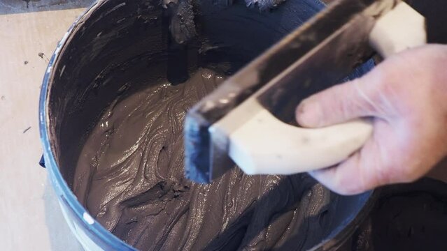 Mixing grey tile grout in a bucket container and then applying to a tile float or spreader. Concept for tiling, DIY, home renovation and improvements.