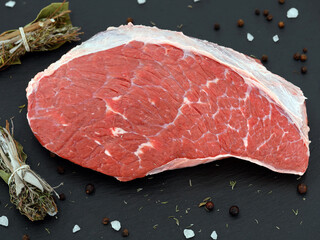 fresh raw rump meat cut from the picanha cap on a black slate plate with salt, pepper and bundle of...