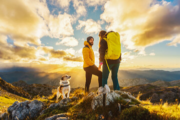couple of mountaineers with their dog watching the sunset after hiking in the mountains. outdoor...