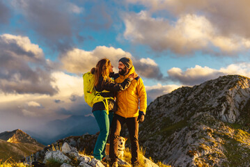 couple of mountaineers in love hug each other on top of a mountain at sunset. hikers with backpacks...