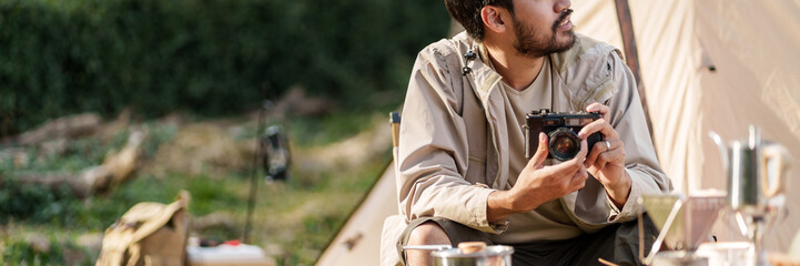 Asian man drinking coffee enjoying camping outdoors in nature. Man traveler hands holding cup of coffee.