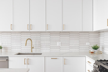 A beautiful kitchen faucet detail with white cabinets, a gold faucet, white marble countertops, and...