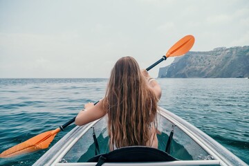 Woman in kayak back view. Happy young woman with long hair floating in transparent kayak on the crystal clear sea. Summer holiday vacation and cheerful female people relaxing having fun on the boat - obrazy, fototapety, plakaty