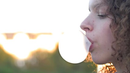 Curly-haired teenage girl inflates a big gum bubble until it bursts.