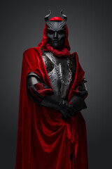 Portrait of dark knight with red robe and black mask isolated on gray background.