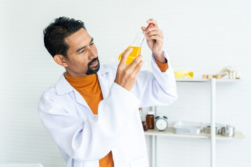Male teacher in white lab coat with safety glasses using pipette carefully transfer the chemical liquid required volume thoroughly with laboratory tools background in university science classroom.