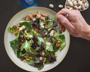 cook placing ingredients with tongs into a healthy salad top view