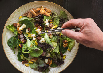 cook placing ingredients with tongs into a healthy salad top view