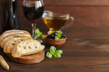 Sliced ciabatta with red wine, olive oil, olives and basil on a wooden background.