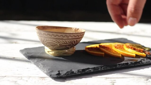 hand placing mezcal shot in traditional bowl and taking orange slice