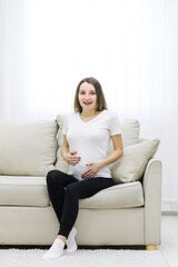 Pregnant woman wearing white t-shirt touching her stomach.