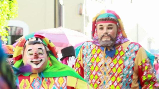 group of male mexican dancers dressed as clowns, wearing very bright and colorful costume wooden mask performing a dance during  the mexican carnival