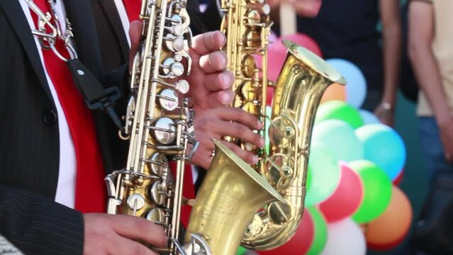 close up of hands of two mexican hispanic musicians wearing black suits playing wind instruments, saxophone