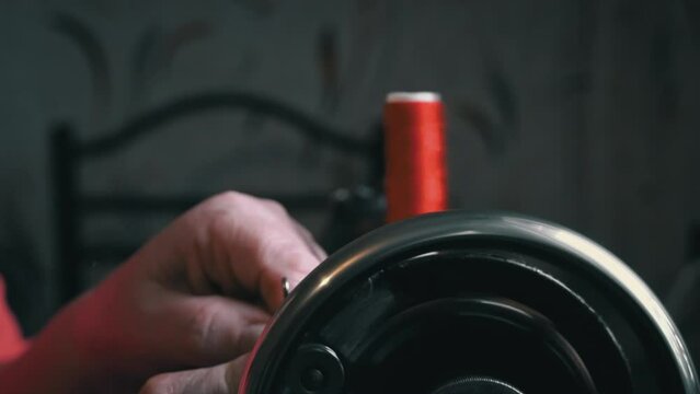Woman winds a thread for sewing on a typewriter close-up. An elderly woman in glasses sews on an old sewing machine. A seamstress makes a machine-made even seam on a red fabric.