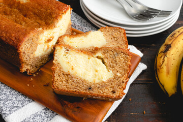 Sliced Cream Cheese-Filled Banana Bread on a Wooden Cutting Board: Slices of banana bread with ripe bananas in the background