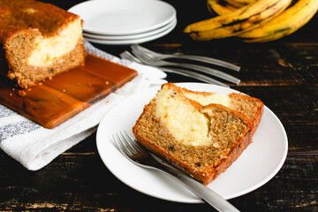 Slices of Cream Cheese-Filled Banana Bread on a White Plate: Slices of banana bread with ripe bananas in the background