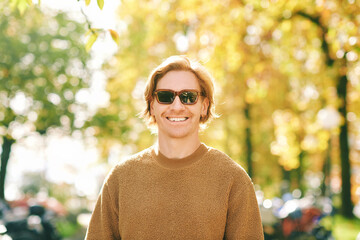 Outdoor autumn portrait of handsome young man wearing brown fuzzy fleece sweater and sunglasses