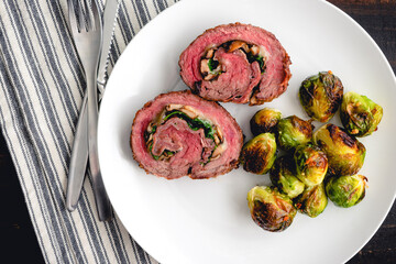 Stuffed Flank Steak with Prosciutto and Mushrooms Dinner: Slices of steak roulade served on a plate with roasted Brussels sprouts
